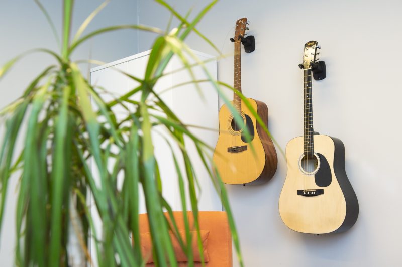 Sisäkuva Breikki Helsingistä. Kuvan etualalla on viherkasvi, mutta kuva on tarkennettu vastakkaisella seinällä roikkuviin kahteen akustiseen kitaraan.