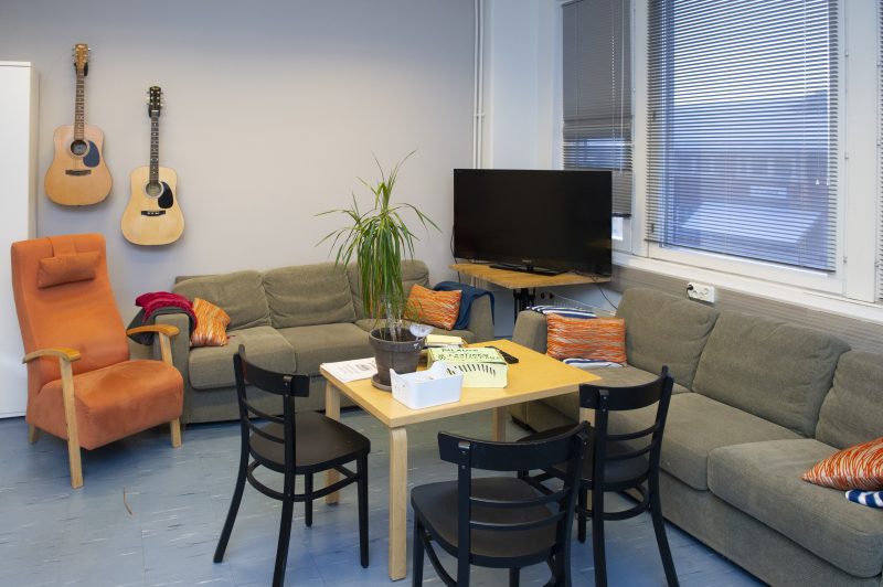 Sisäkuva Breikki Helsingin oluhuoneesta. Kuvassa näkyy kaksi sohvaa, nojatuoli ja televisio. Sohvilla on koristetyynyjä. Seinällä roikkuu kaksi kitaraa.