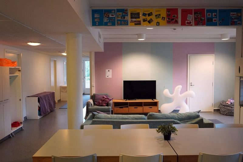 Sisäkuva toimipisteestä. Kuvassa on värikäs seinä, sen edessä televisio ja sohva, etualalla pitkä pöytä jonka ympärillä on tuoleja.