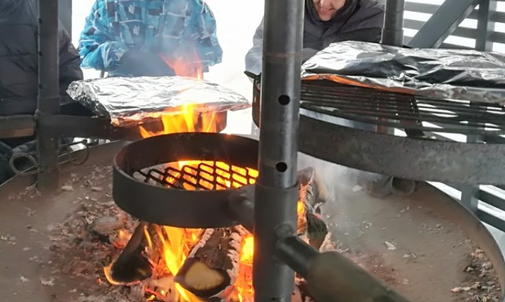 Kuvassa on Kompassin kota, jonka keskellä on nuotio. Nuotion päälle voi kääntää ritilöitä, joilla paistetaan ruokaa. Taustalla näkyy ihmisiä odottamassa ruokien valmistumista.