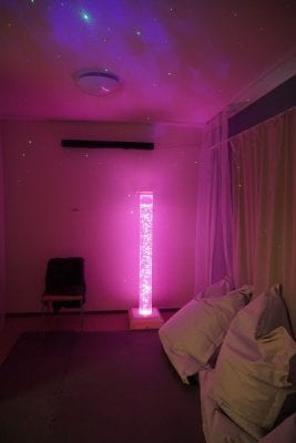 Toimintakeskus Meripihkan aistihuone jossa on pinkki valo ja heijastus katossa. Seinustalla on kaksi säkkituolia.