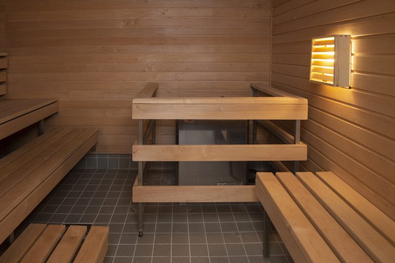 Kuvassa on tilava sauna. Kiukaan ympärillä on aita, lauteita on kolme.