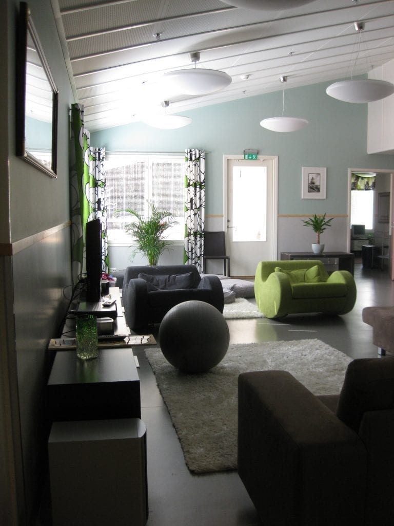 Multatien olohuoneessa on harmaa-vihreä sisustus. Huoneesta löytyy sohva, ja kaksi keinutuolia, jumppapallo, tv-taso ja televisio. Tilassa on mattoja ja viherkasveja.