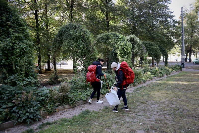 Kaksi ihmistä punaiset reput selässä kerää roskia puistossa.