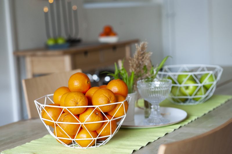 Lähikuvassa ruokailupöytä, jolla on kaksi hedelmäkoria, toisessa on appelsiineja ja toisessa omenia.