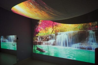 Kuvassa on toimintakeskus Nyyttipuiston aistihuone, jossa on seinille ja kattoon heijastettu värikas vesiputous-maisema.