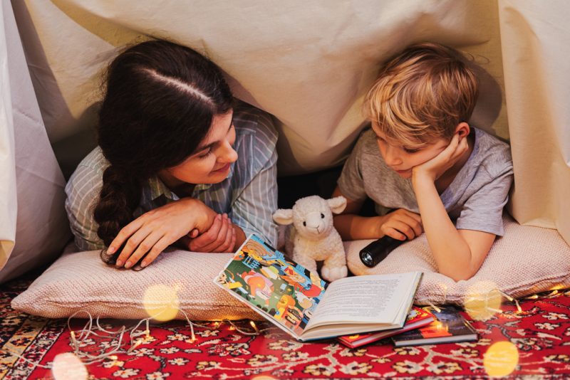 aikuinen ja lapsi lukevat kirjaa majassa taskulampun valossa