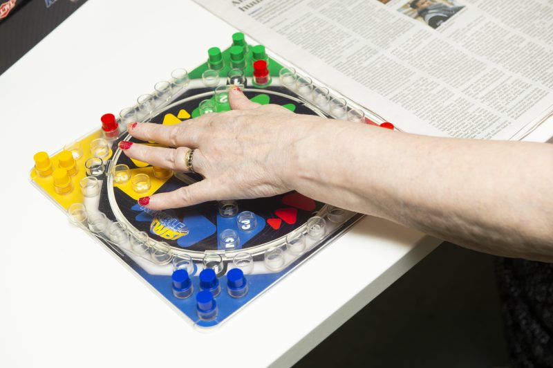 Kuvassa on pöytä, jolla on sanomalehti sekä Kimble-peli. Käsi on painamassa Kimblen keskinappulaa.