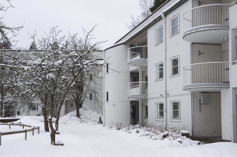 Kuvassa on valkoinen, kolmekerroksinen asuinrakennus lumisessa maisemassa.