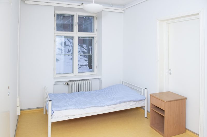 Huonekuva Tammituvasta. Asumattomassa huoneessa on ikkuna, sänky ja yöpöytä. Seinät ovat valkoiset.