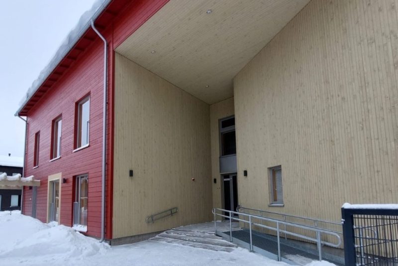 Ulkokuva Vehkasta. Rakennus on punaiseksi maalattua puuta, paitsi pääoven luota seinät on jätetty puunväriseksi. Maassa on lunta.