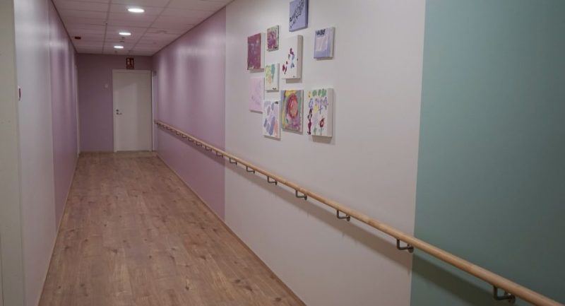 Sisäkuva toimipisteen käytävästä. Käytävän seinät on maalattu valkoiseksi, vaaleanpunaiseksi ja turkoosiksi. Seinällä pieniä tauluja.