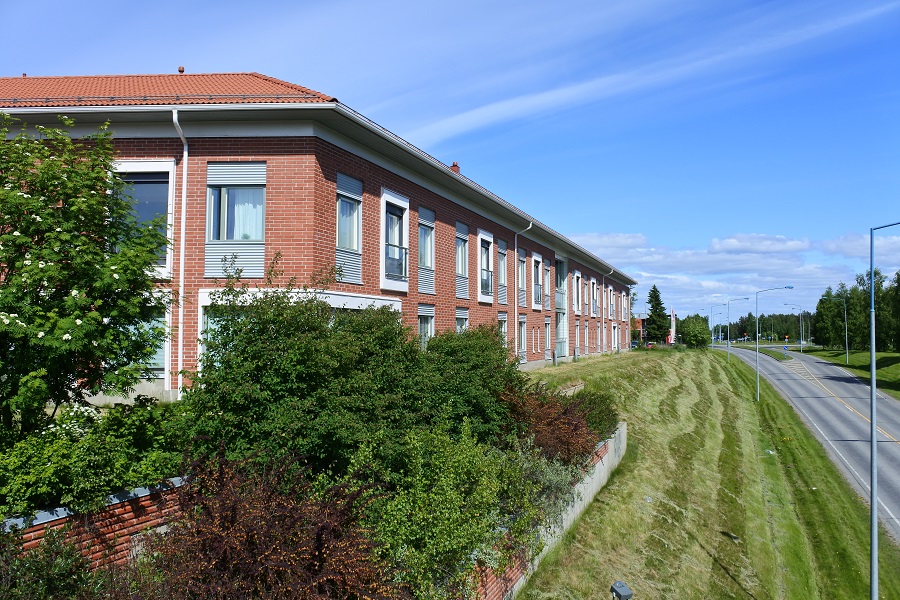 Julkisivukuva Nestorista. Rakennus on punatiilinen kaksikerroksinen talo, jossa on ranskalaisia parvekkeita. Rakennuksen vieressä on nurmikkoinen alamäki ja sen vieressä maantie.
