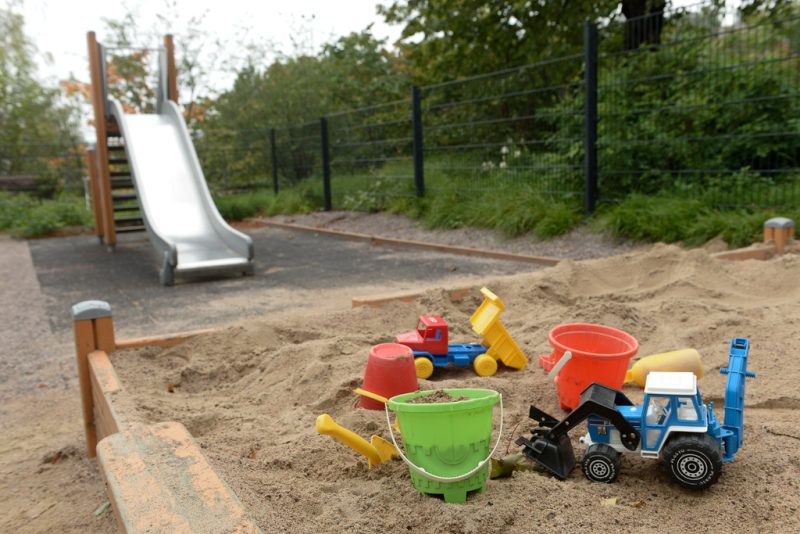 Ulkokuva leikkipuistosta. Taustalla näkyy liukumäki, etualalla hiekkalaatikko, jossa hiekkaleluja kuten ämpäreitä ja traktoreita.