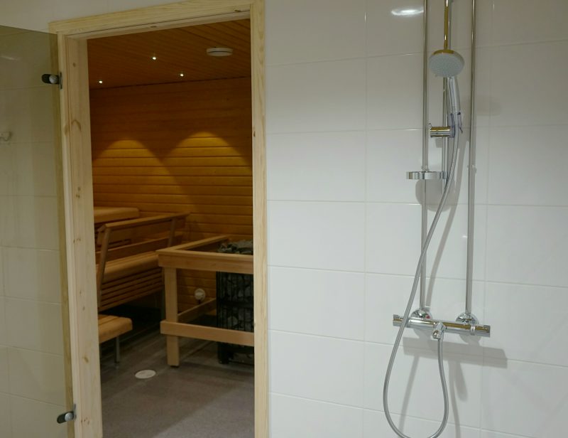 Suihkutila, josta näkyy lasioven kautta saunatilaan.