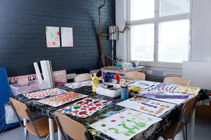 Askartelutilassa pöydällä värikkäitä maalauksia ja maalaustarvikkeita.