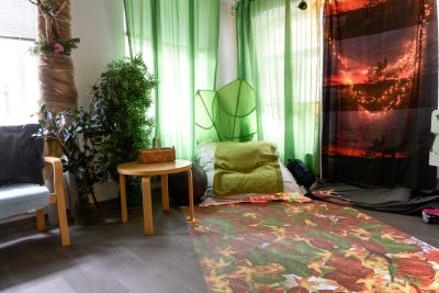 Vihreänsävyinen kuva, jossa seinustalla vihreiden verhojen edessä lattialla säkkituoli. Lisäksi huoneessa jumppapallo ja pieni pöytä. Lattialle heijastuu syksyn lehtiä eri väreissä.
