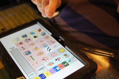 Henkilö on painamassa sormellaan tablettia, jossa on kuvakommunikaatiota.