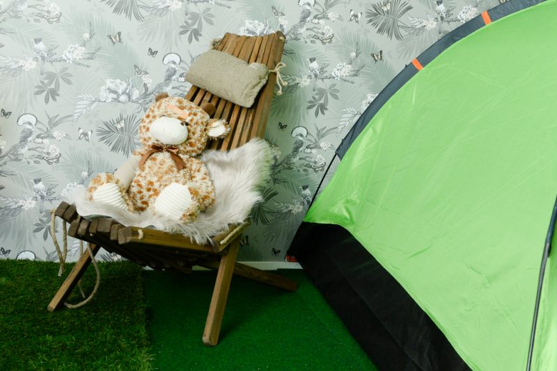 Puinen rantatuoli, jonka päällä karvainen talja ja pehmonalle. Huoneen nurkassa vaaleanvihreä teltta.
