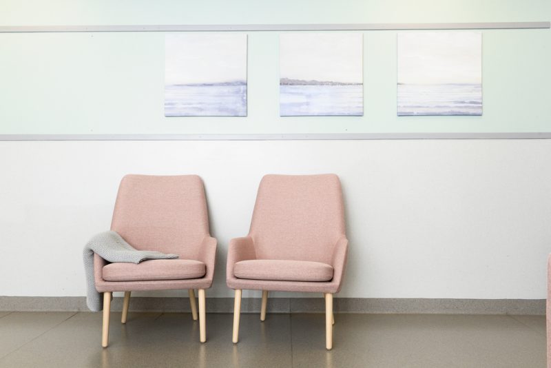 Kaksi vaaleanpunaista nojatuolia seinän edessä. Seinällä kolme erillistä maalausta, jossa merimaisemaa.