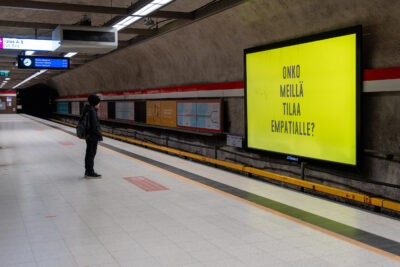 Lapsi seisoo metrolaiturissa ja katsoo keltaista näyttöä, jossa lukee Onko meillä tilaa empatialle?