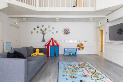 Oleskelutilassa harmaa sohva sekä seinustalla lasten leikkivälineitä.