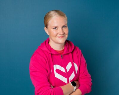 Pinkkiin Rinnekotien brändihuppariin pukeutunut nainen katsoo kameraan hymyillen.