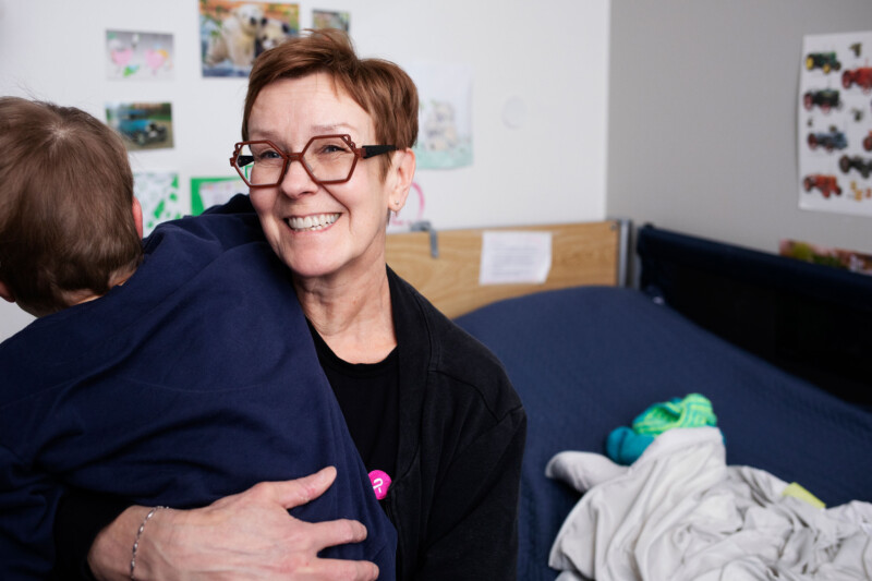 Nainen, jolla paidassaan pinkki Rinnekodit-logo halaa lasta, joka kuvassa selin kameraan.