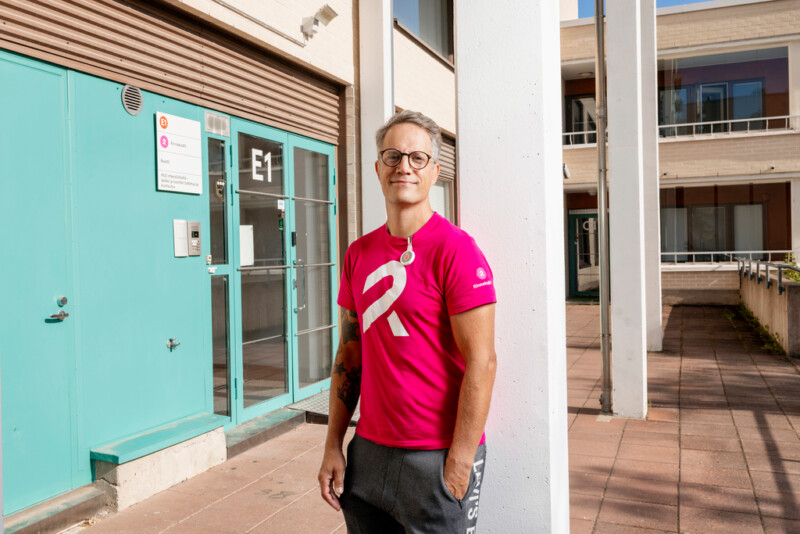 Mies Rinnekotien pinkissä T-paikassa seisoo ulkona katsoen kameraan.