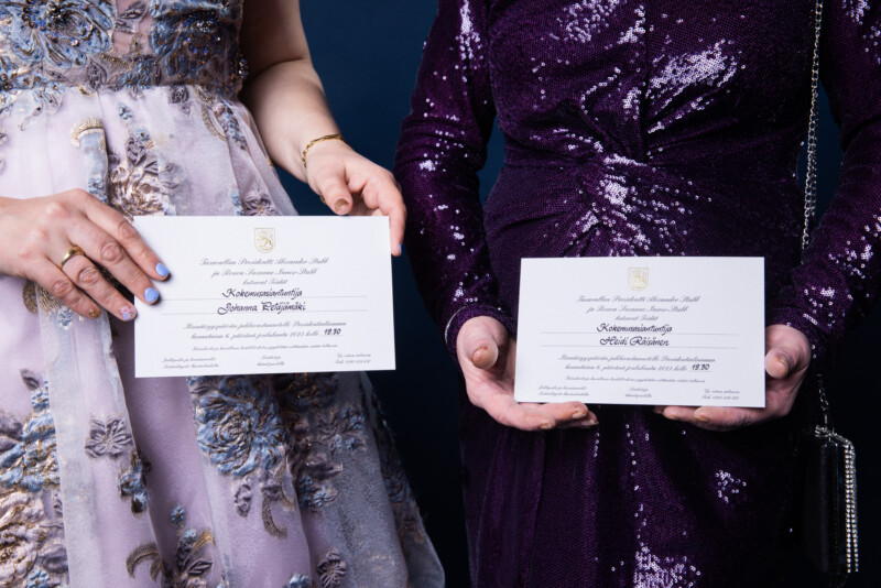 Kaksi naista pitää käsissään Presidentin itsenäisyyspäivän juhlien kutsuja, kasvot rajattu pois kuvasta.