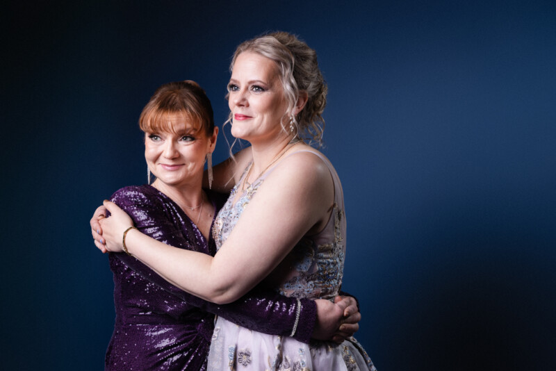 Kaksi naista juhlapuvuissa halaa toisiaan.