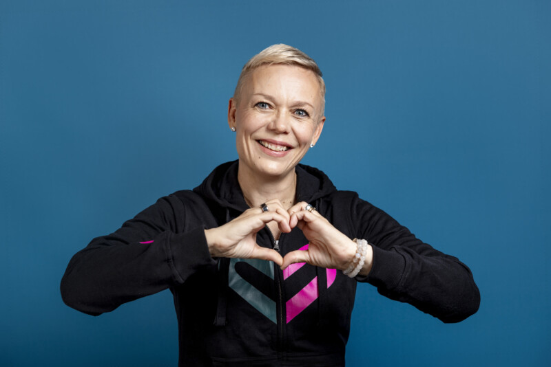Nainen muodostaa käsillään sydämen kohti kameraa, päällään Rinnekotien sydänpaita.