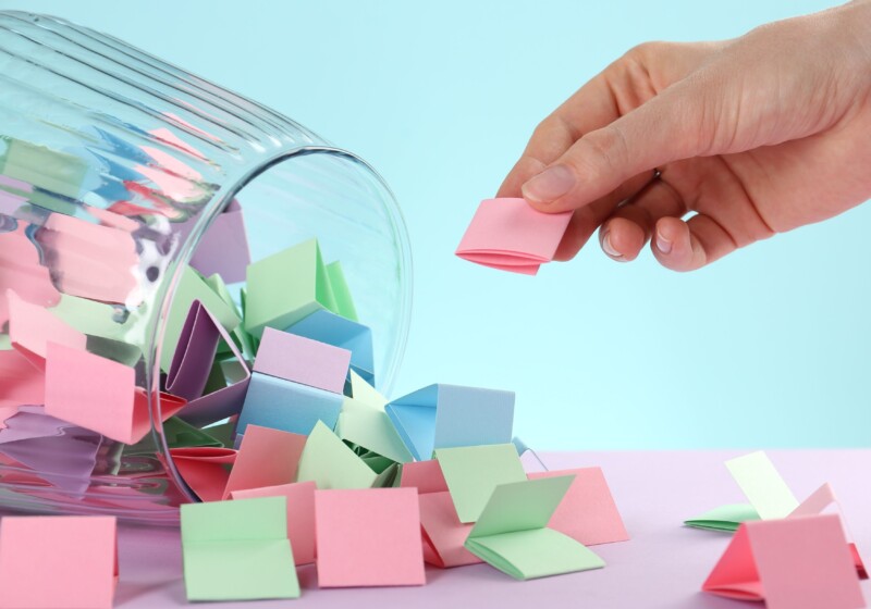 Käsi nostaa värikkäitä lappuja pöydälle kaatuneesta lasikulhosta.