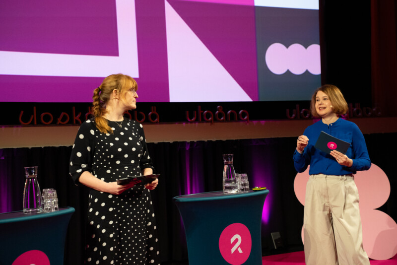 Kaksi henkilöä puhumassa esiintymislavalla.