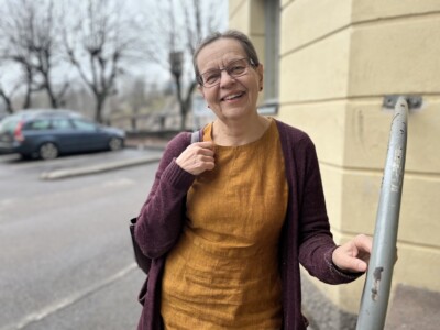 Nainen seisoo ulkona nojaten keltatiiliseen rakennukseen.