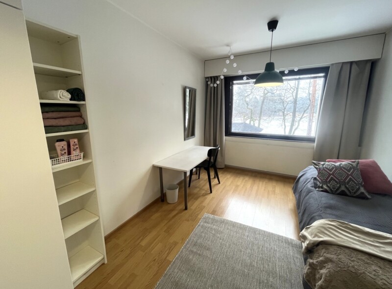 Huone, jossa sänky, kirjoituspöytä ja kirjahylly.