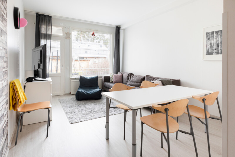 Oleskelutila, jossa pöytä, jonka ympärillä neljä puista tuolia. Takana musta sohva ja säkkituoli sekä televisiotason päällä taulu-tv.