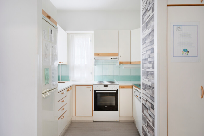 Kapea keittiö, jossa vihreän sävyiset kaakelit, muuten keittiö on vaalean sävyinen.