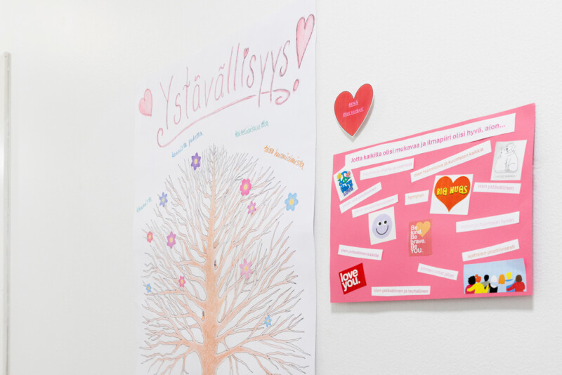 Seinälle kiinnitettyjä askarreltuja tauluja, jossa sanoja ja ajatuksia liittyen ystävällisyyteen ja siihen, että kaikilla olisi mukavaa ja ilmapiiri olisi hyvä.