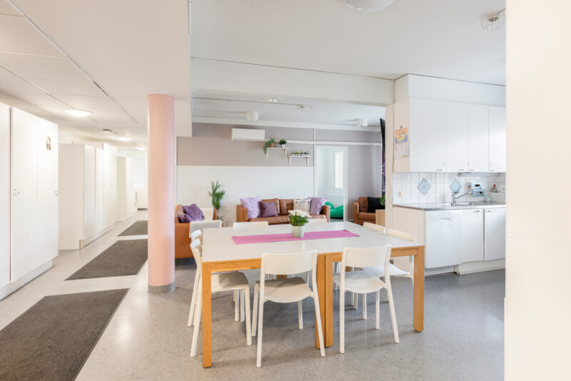 Keittiössä käytävän vieressä kahdeksan henkilön ruokailupöytä tuolineen. Taustalla näkyy oleskelutilaa.