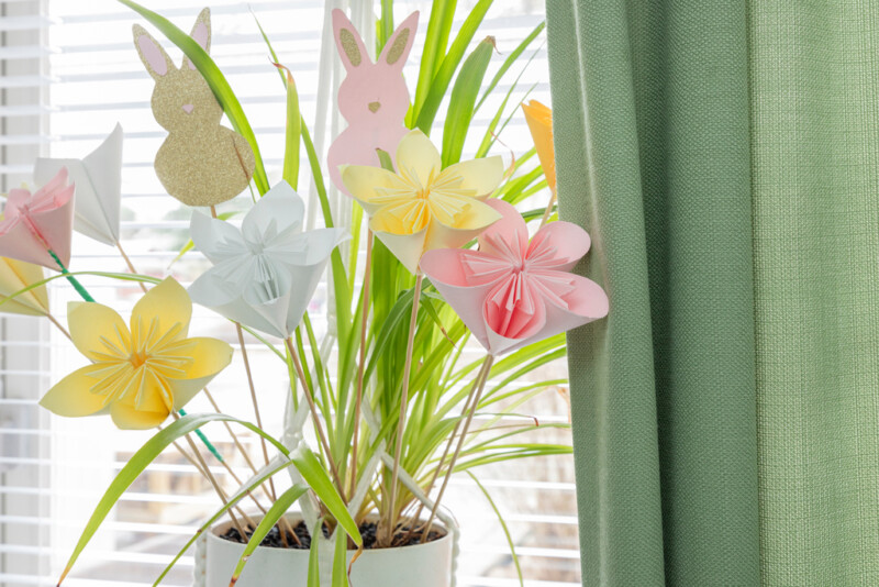 Ikkunalaudalla viherkasvin seassa askarreltuja paperikukkia.