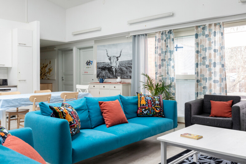 Oleskelutilassa sinisen värinen sohva ja musta nojatuoli. Takana näkyy ruokailutilaa.