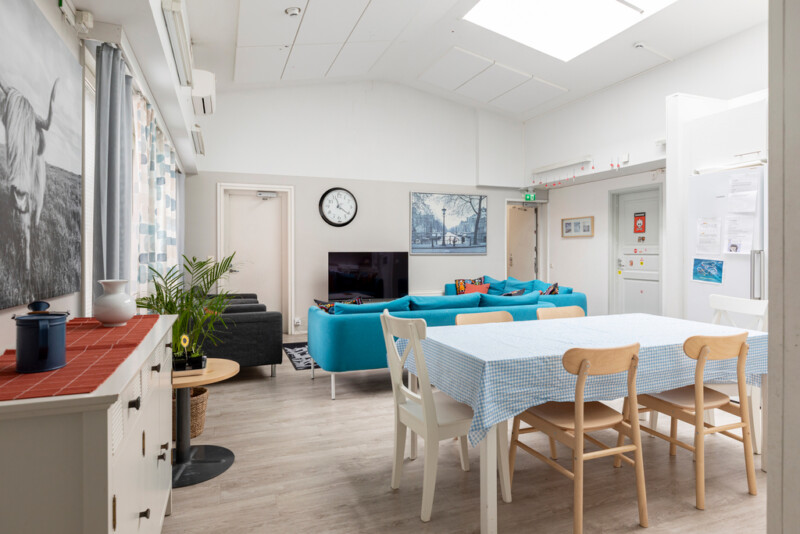 Oleskelutila ja ruokailutila yhdistyvät yhdeksi huoneeksi. Oleskelutilassa sohva-alue television ympärillä, etualalla ruokailupöytä.