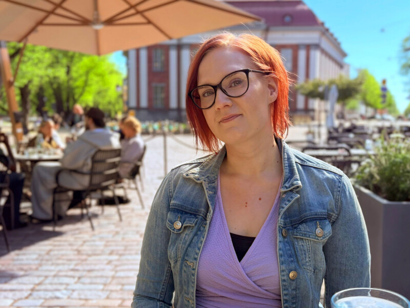 Henkilö istuu terassila aurinkoisena päivänä ja katsoo kameraan.