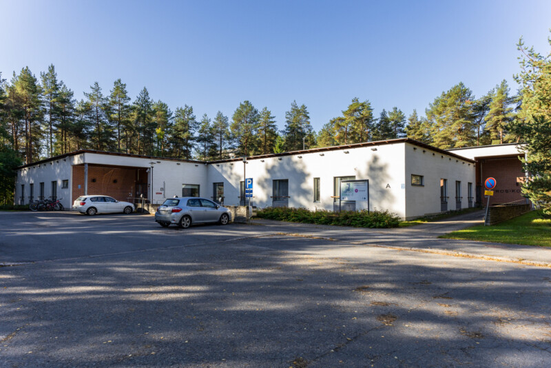 Yksikerroksinen matala rakennus, jonka edustalla parkkipaikka.