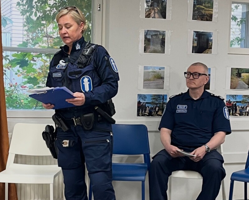 Naispoliisi puhuu yleisölle sininen kansio käsissään, miespoliisi istuu taustalla.