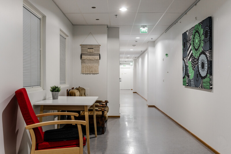Pitkä käytävä, jonka varrella on pöytä, nojatuoleja ja seinätekstiilejä.