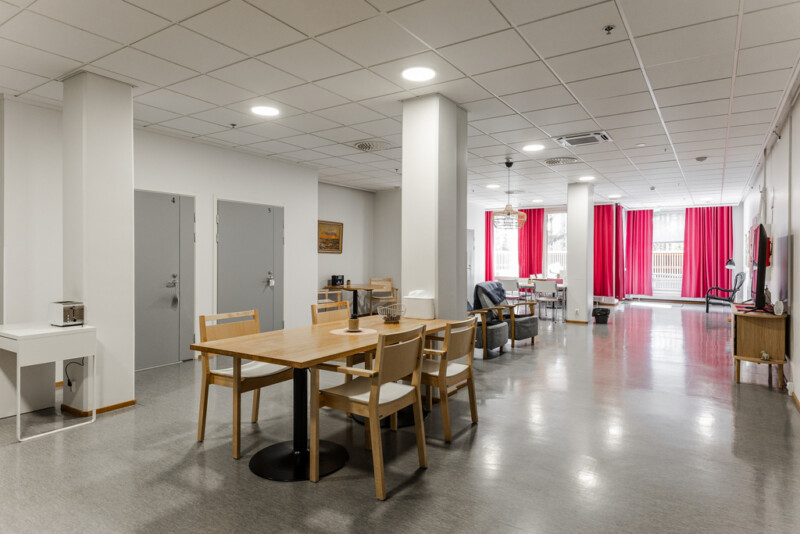 Avara yhteinen oleskelu- ja ruokailutila, jossa on puinen ruokapöytä, nojatuoleja ja suuret ikkunat.