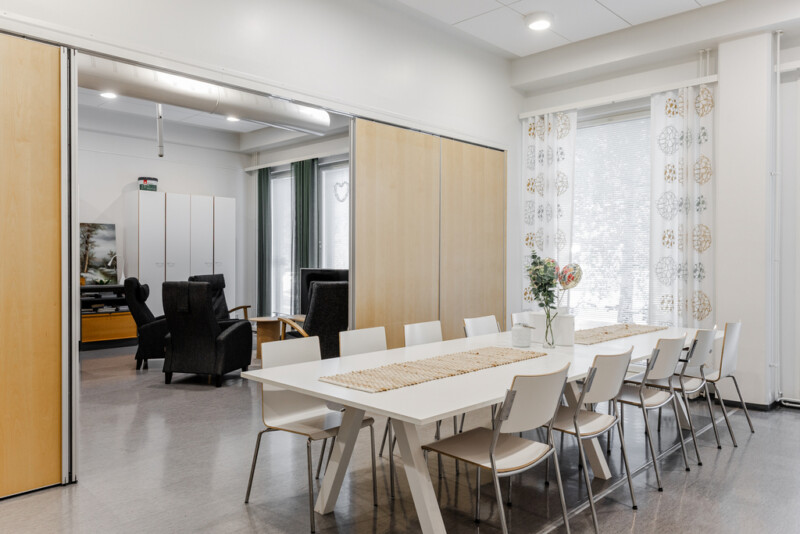 Valoisa ruokailutila, jossa on pitkä pöytä tuoleineen ja vieressä oleskelutila.